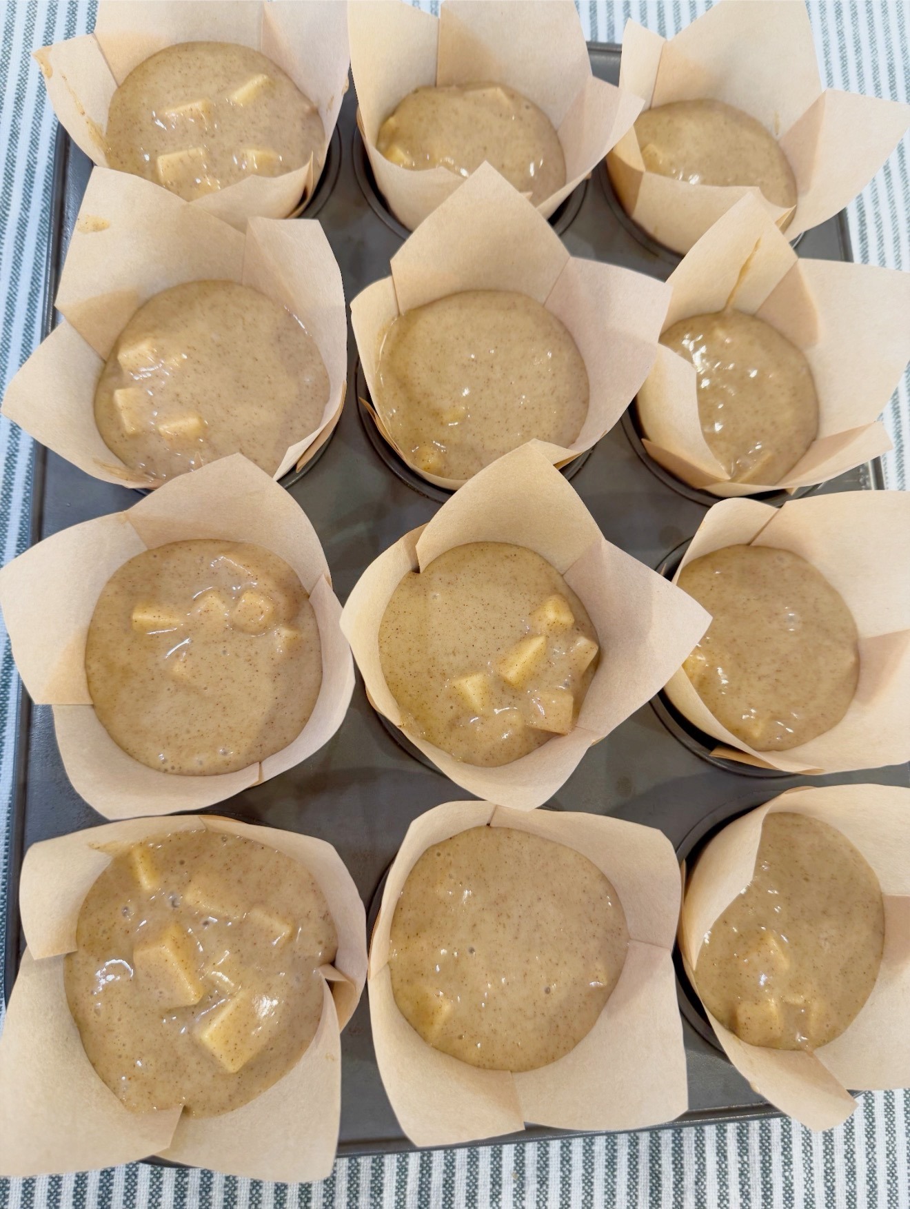 Muffin pan filled with apple batter in parchment liners