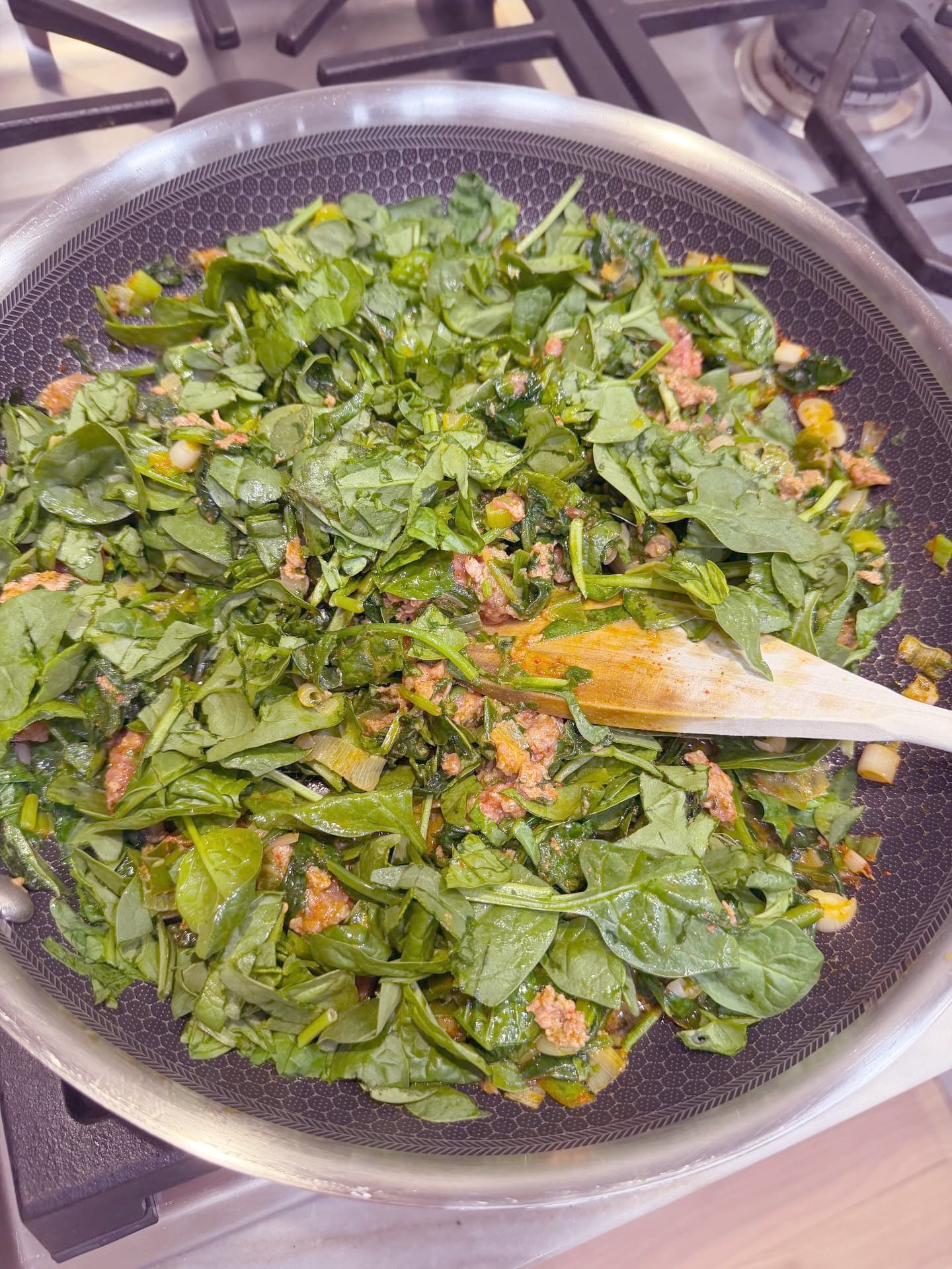 Adding chopped fresh spinach to the browned ground meat in the skillet