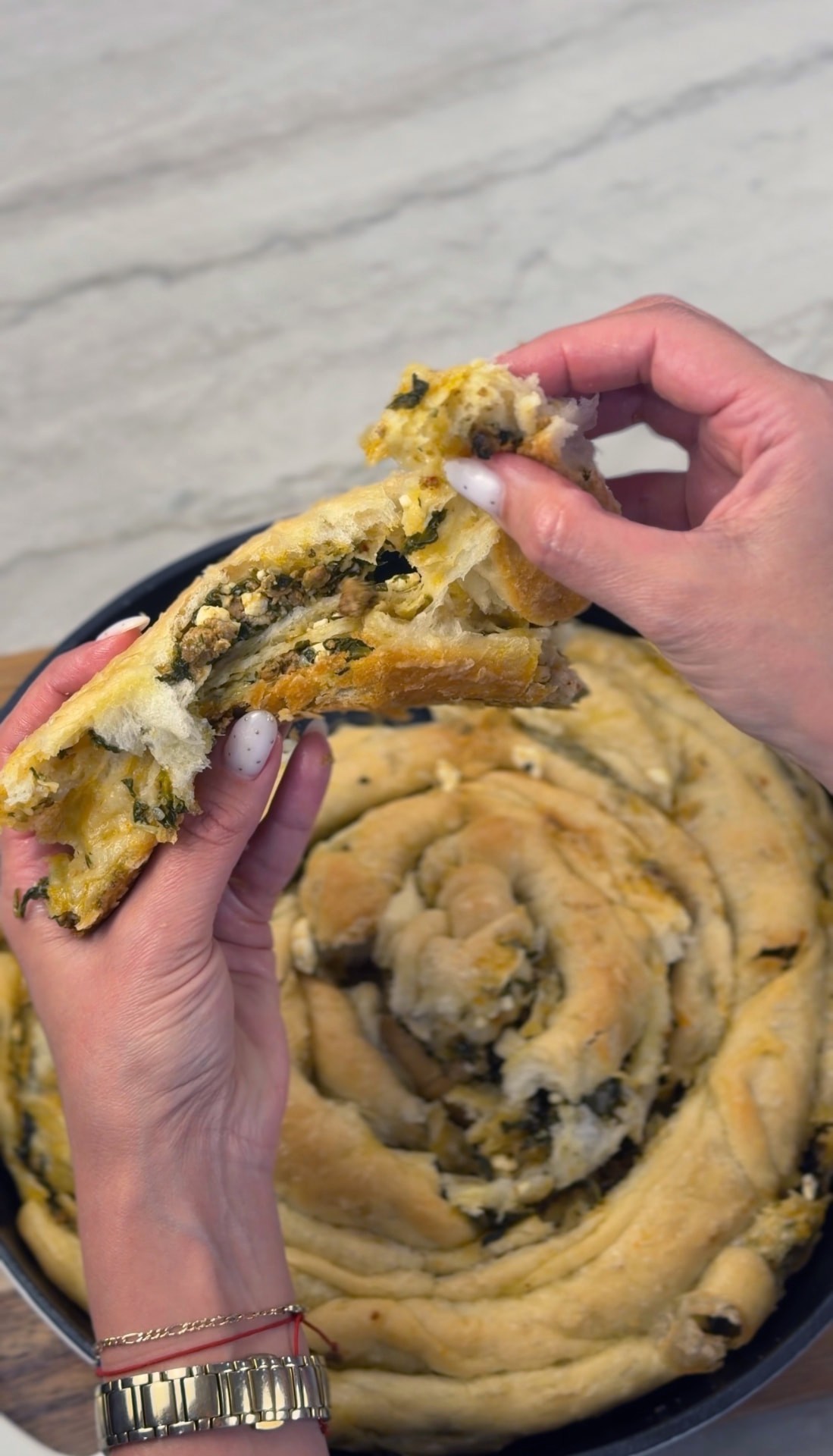 A piece pulled from the warm banitsa, showing the meat, spinach, and feta filling