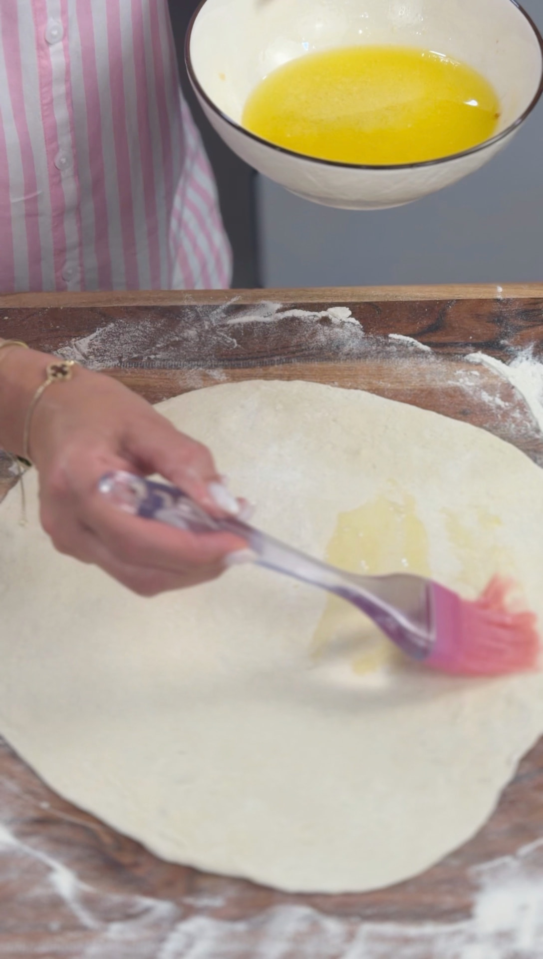 Brushing the rolled dough with melted butter, a bowl of butter alongside