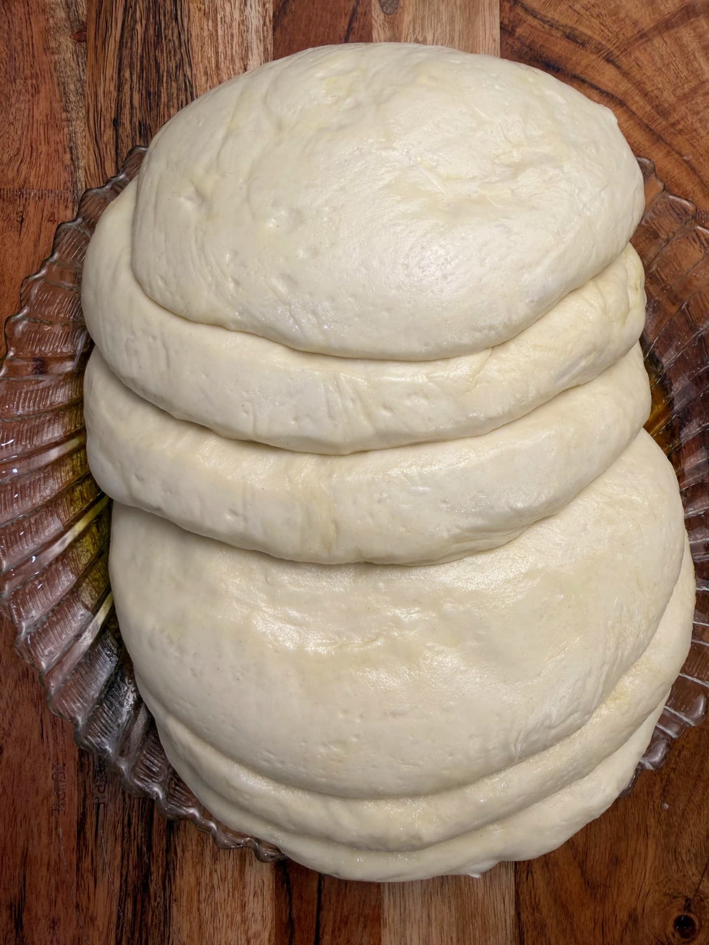 Oiled dough disks stacked on a glass plate, resting before stretching