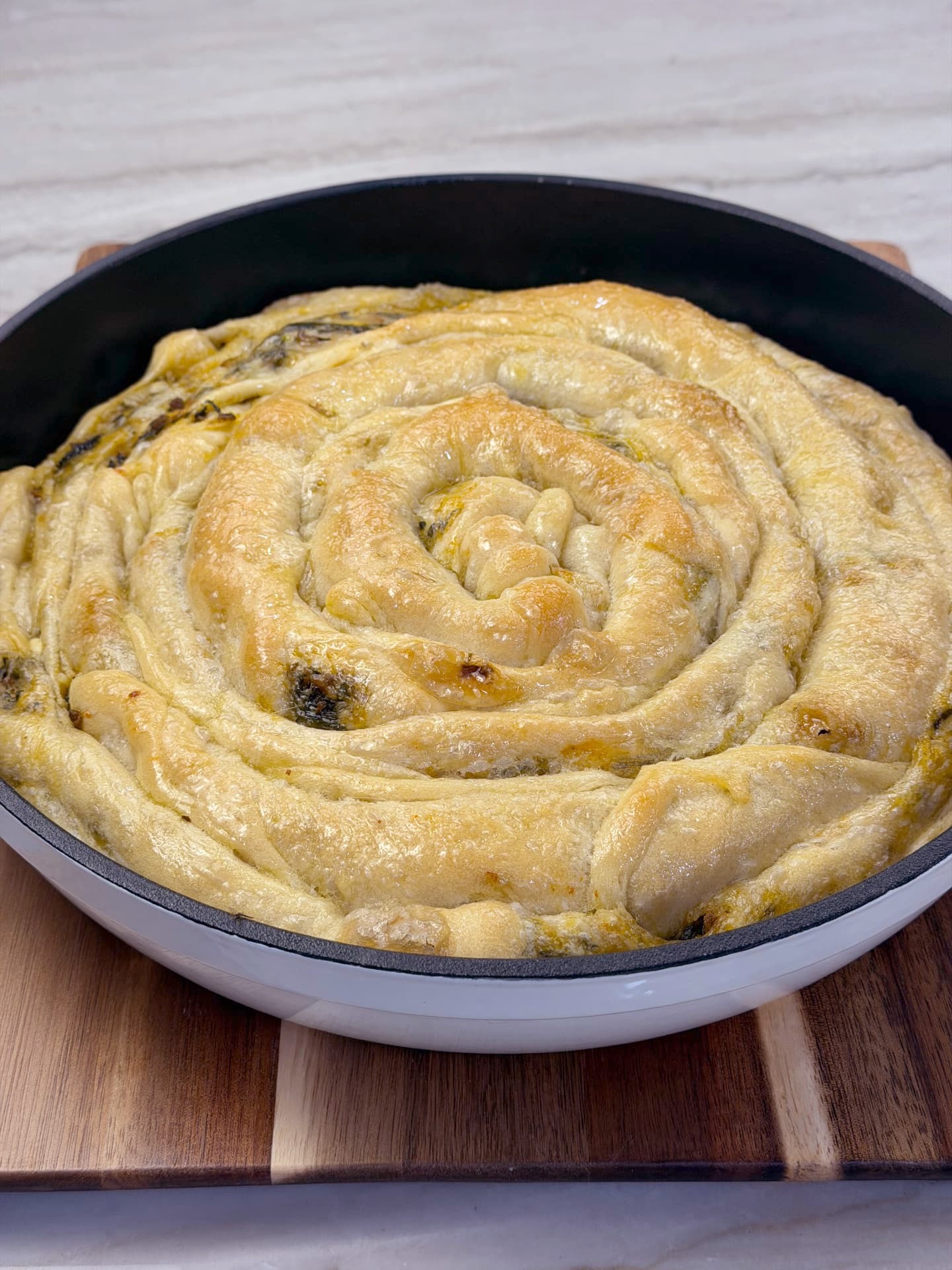 The finished banitsa spiral in its round pan on a wooden board