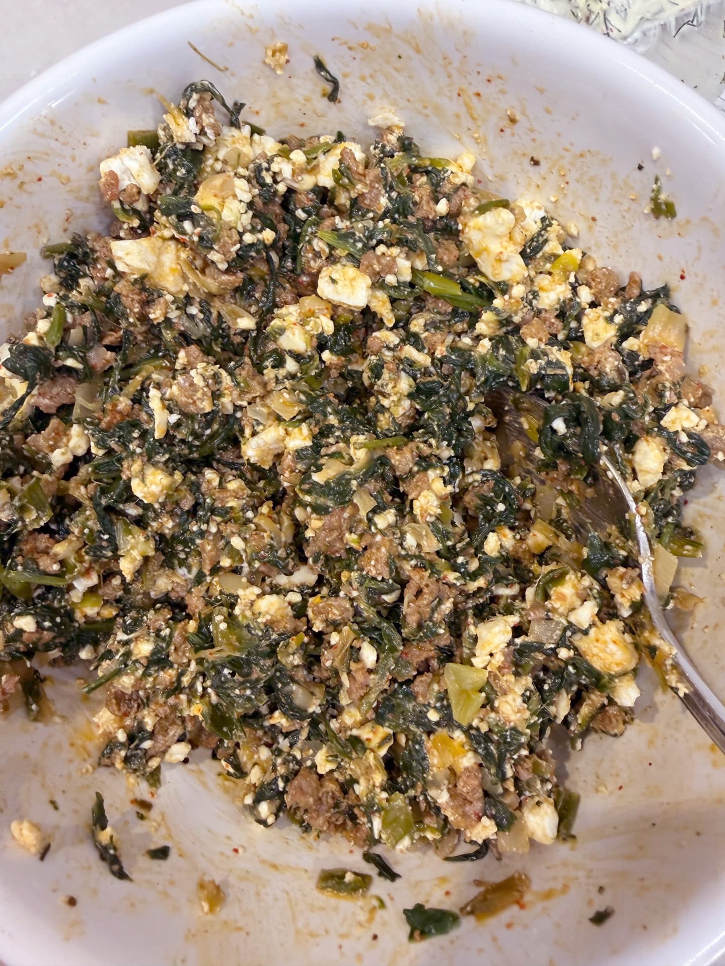 The cooked meat and spinach filling in a bowl with crumbled feta mixed in