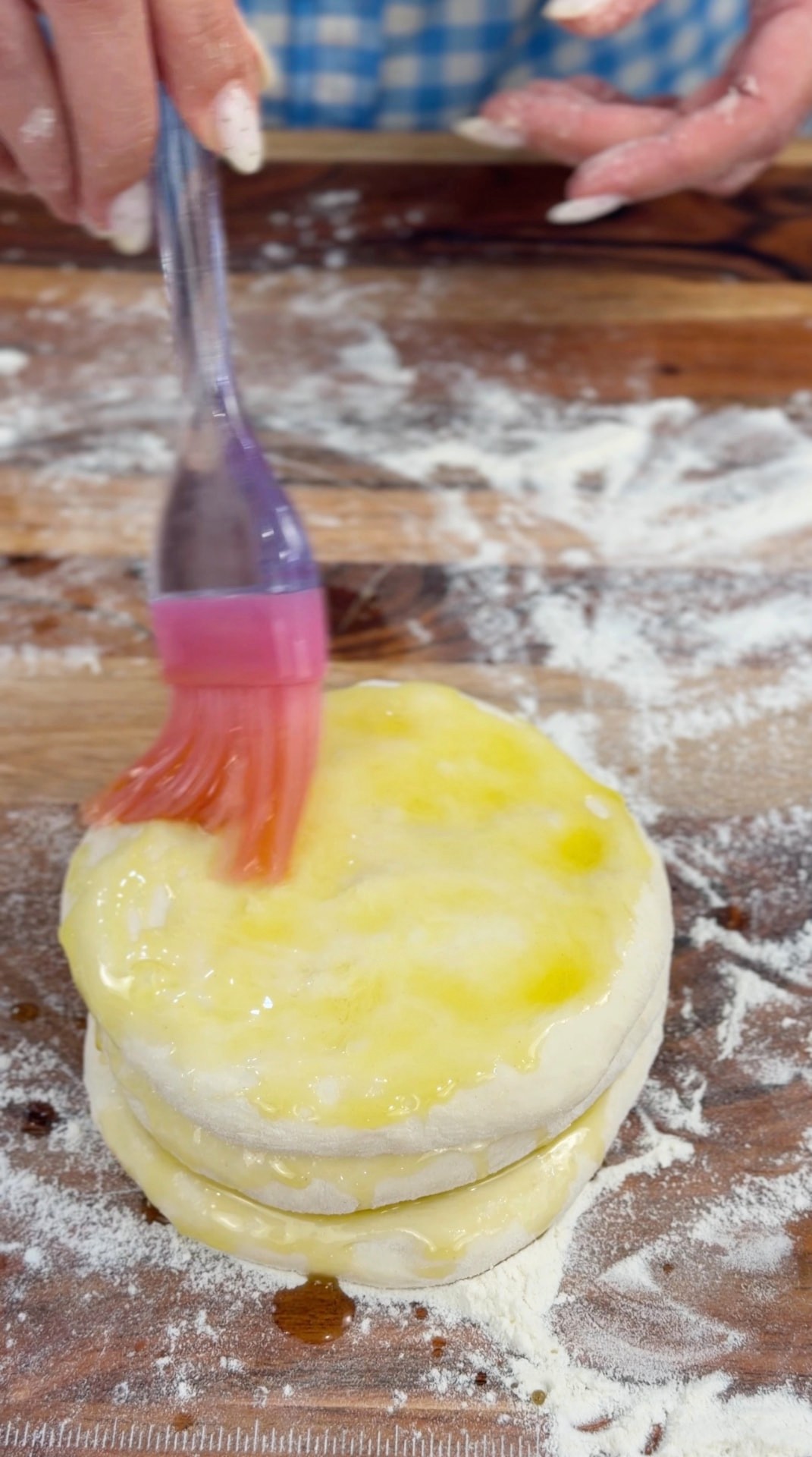 Brushing melted butter over the stacked dough disks with a pastry brush
